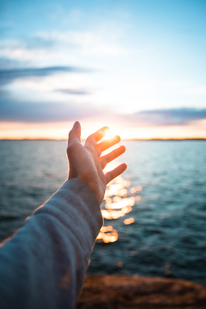 Man's outstretched hand towards the sun across the water